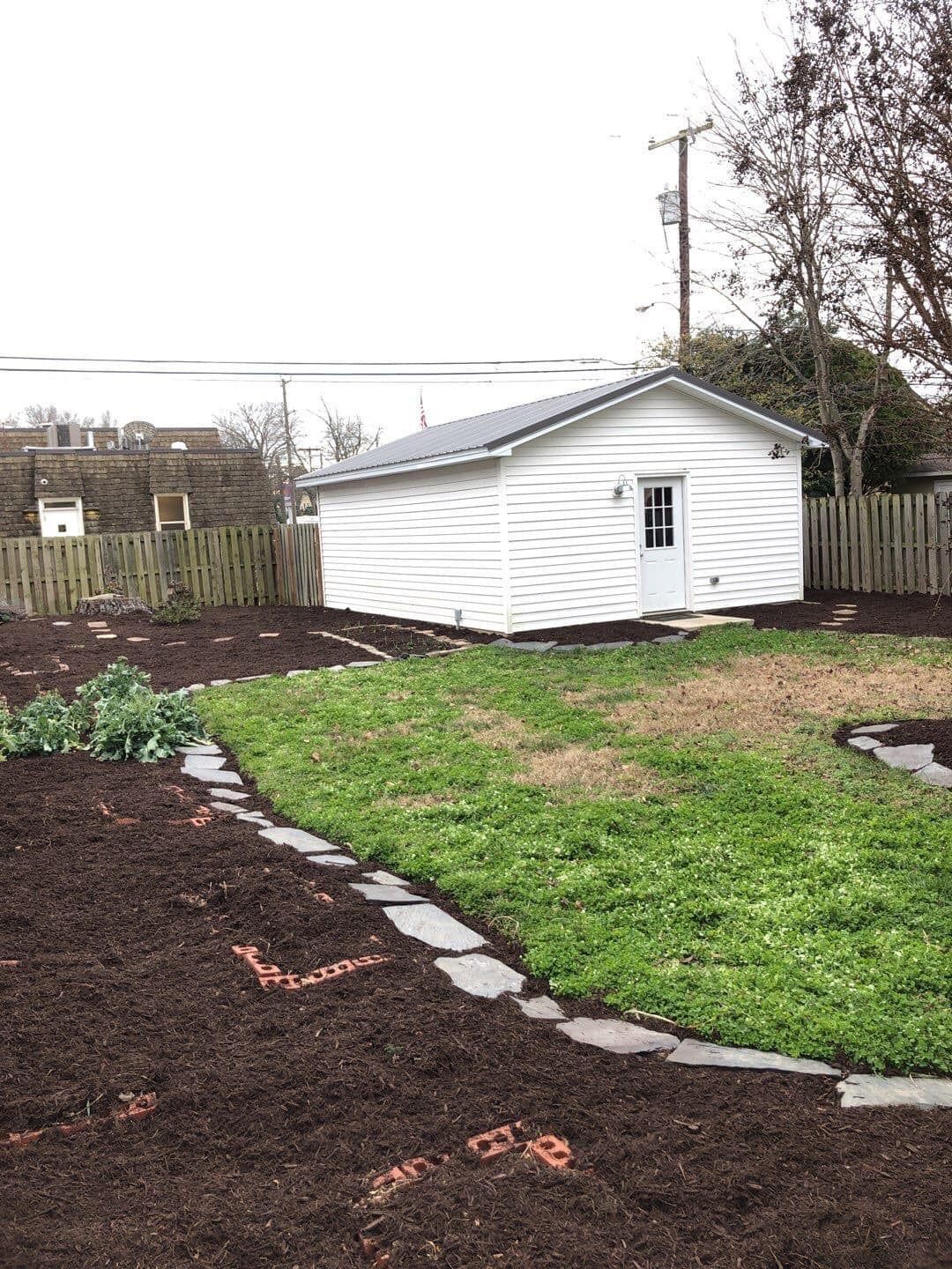 A white shed is sitting in the middle of a lush green yard.