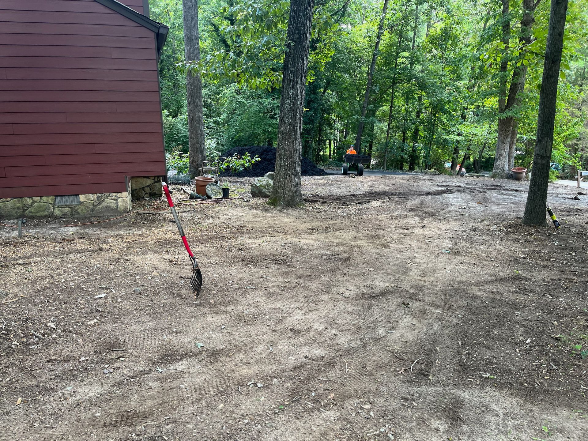 A shovel is sitting in the dirt in front of a house in the woods.