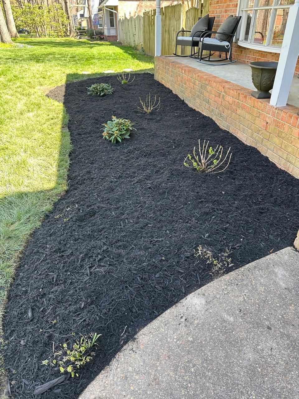 A lawn with black mulch and plants in front of a house.