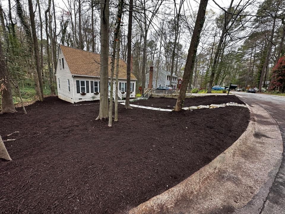A white house is surrounded by trees and mulch.