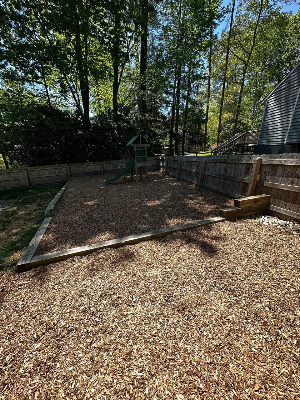 A backyard with a playground and a fence surrounded by trees.