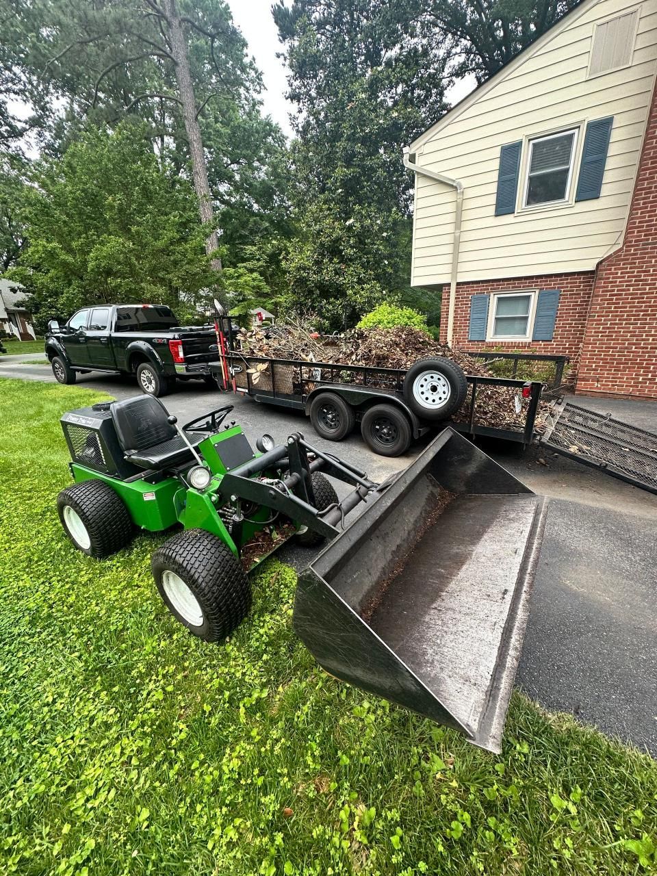 A green lawn mower is parked in front of a house next to a trailer.