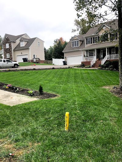 A lush green lawn with a yellow pole in the middle of it in front of a house.