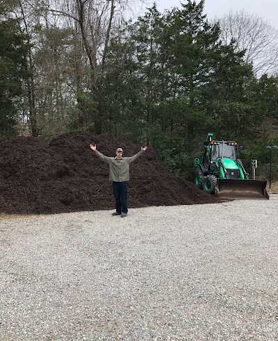 A man is standing in front of a pile of mulch and a bulldozer.