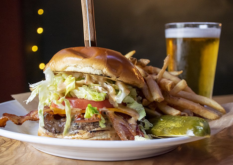 Burger with bacon, lettuce, tomato, and sauce, fries, a pickle, and beer.