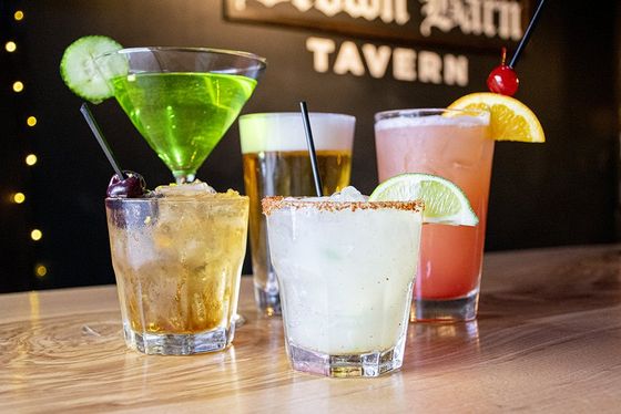 Assortment of cocktails on a bar top. Includes a green martini, beer, margarita, and a tall pink drink.