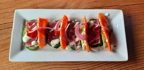 Appetizer with sliced cucumbers, tuna, carrot sticks, and red onion on a white plate.