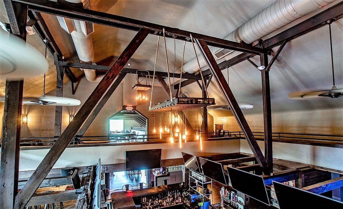 Interior view of a bar with exposed beams, overhead lighting, and a partial view of the bar below.