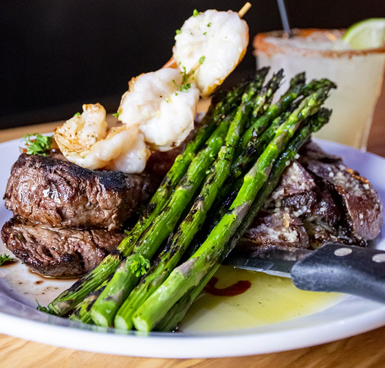 Steak with shrimp skewer and asparagus on a plate, margarita in the background.