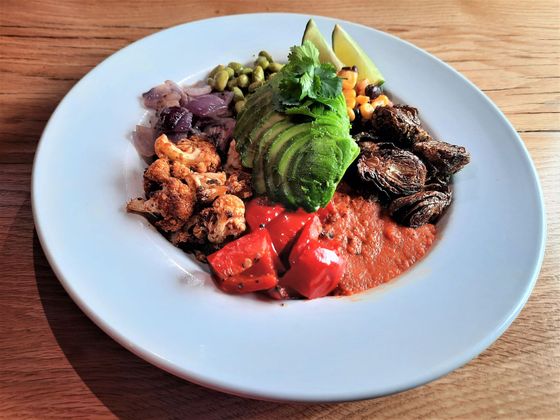 A colorful bowl with avocado, roasted vegetables, and a creamy sauce.