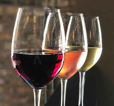Four wine glasses filled with red, rosé, and white wine in front of a brick background.