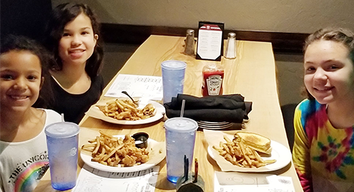 Four smiling children at a restaurant table with fries and food.