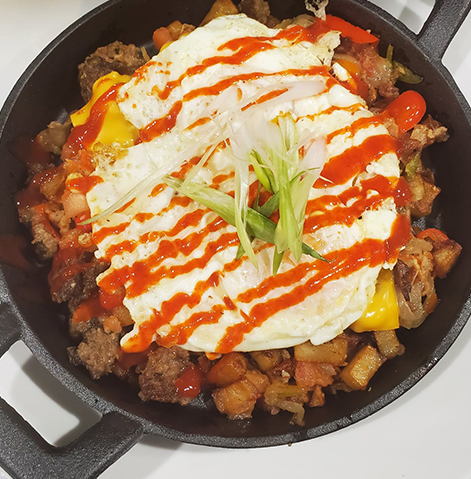 Breakfast hash with egg and hot sauce in a cast iron pan.