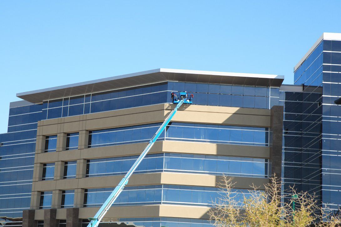 A man on a crane is cleaning the windows of a building