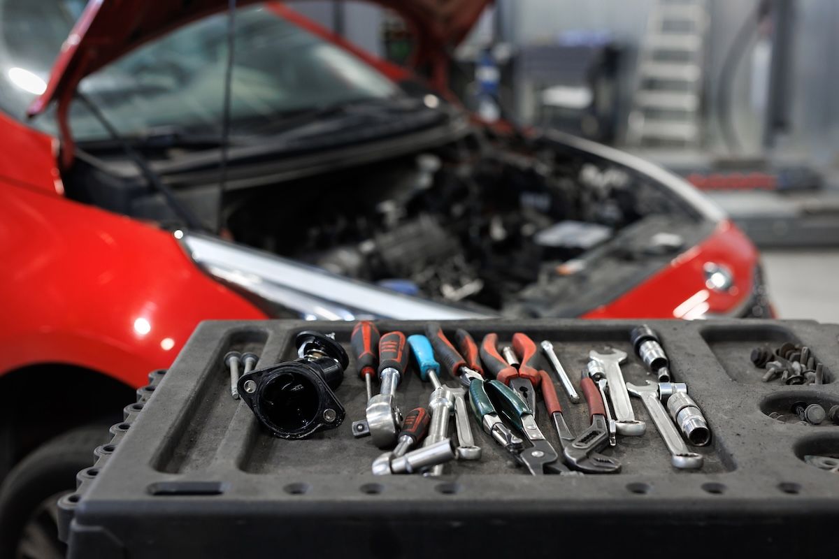 Red car with open hood in a garage, with a tool tray of wrenches and pliers in the foreground