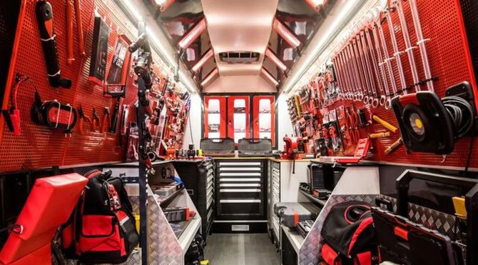Red fire truck interior with organized firefighting gear, hoses, tools, and rear doors open at the back.