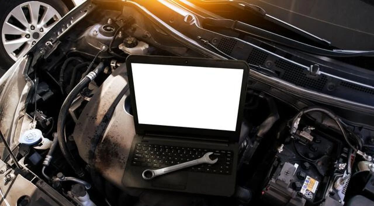 Laptop on a car engine bay with a wrench, suggesting vehicle repair diagnostics