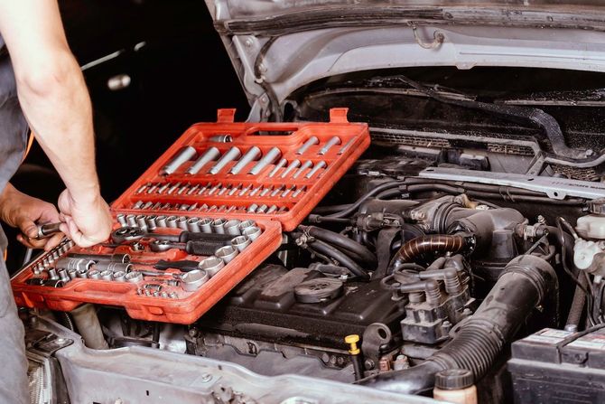 Person using a red tool kit to repair a car engine under an open hood