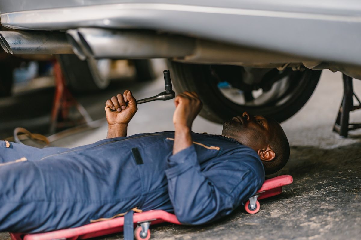 Mechanic lying under a car, using a wrench to work on the underside in a garage.