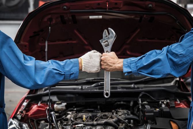 Mechanic holding a wrench over an open car engine bay with the hood raised