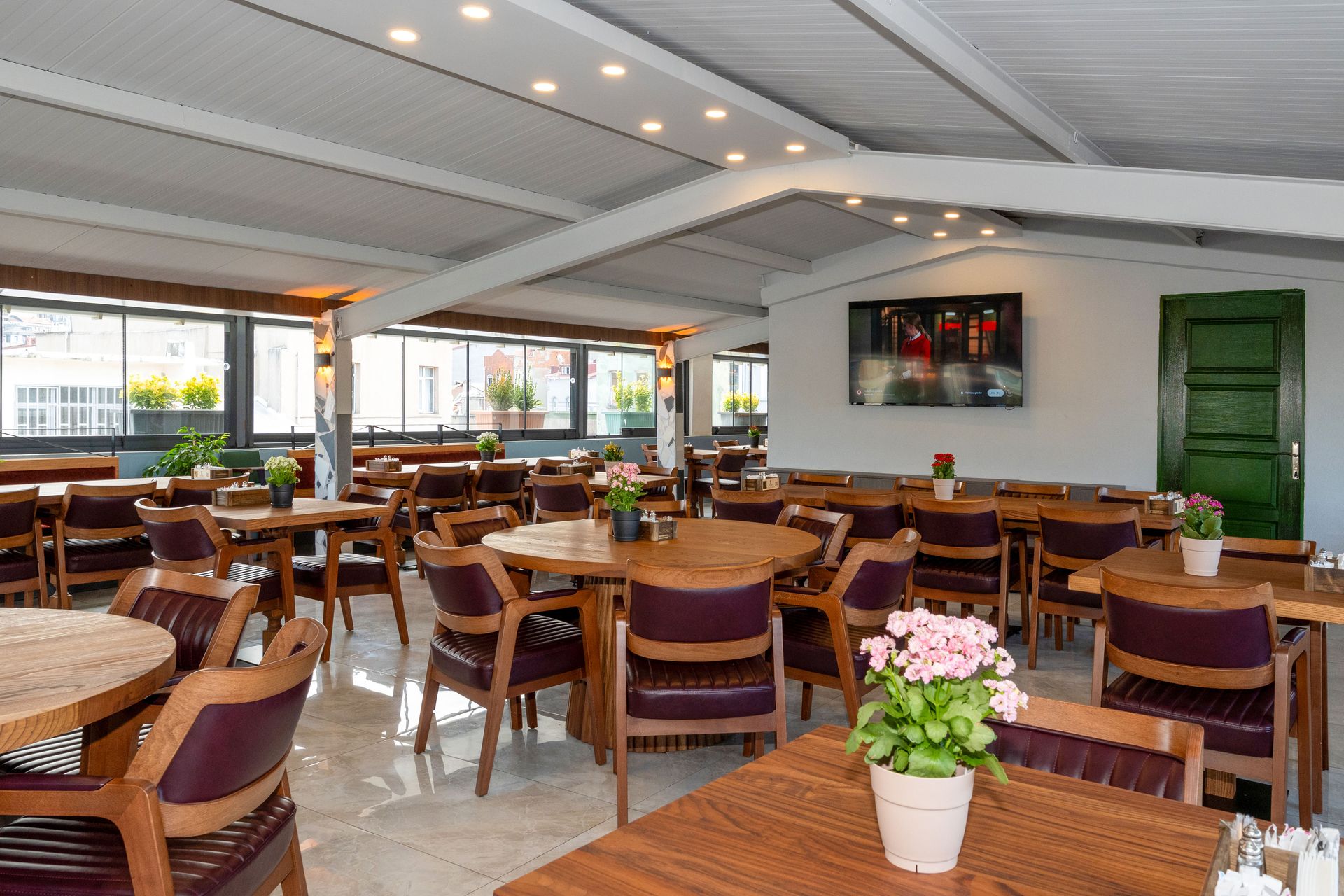 Mays Otel | Restaurant interior with wooden tables and chairs, white ceiling, and potted flowers.