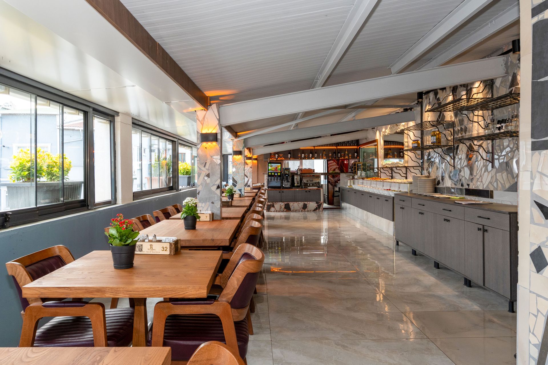 Mays Otel | Restaurant interior with wooden tables, chairs, and bar; bright lighting.