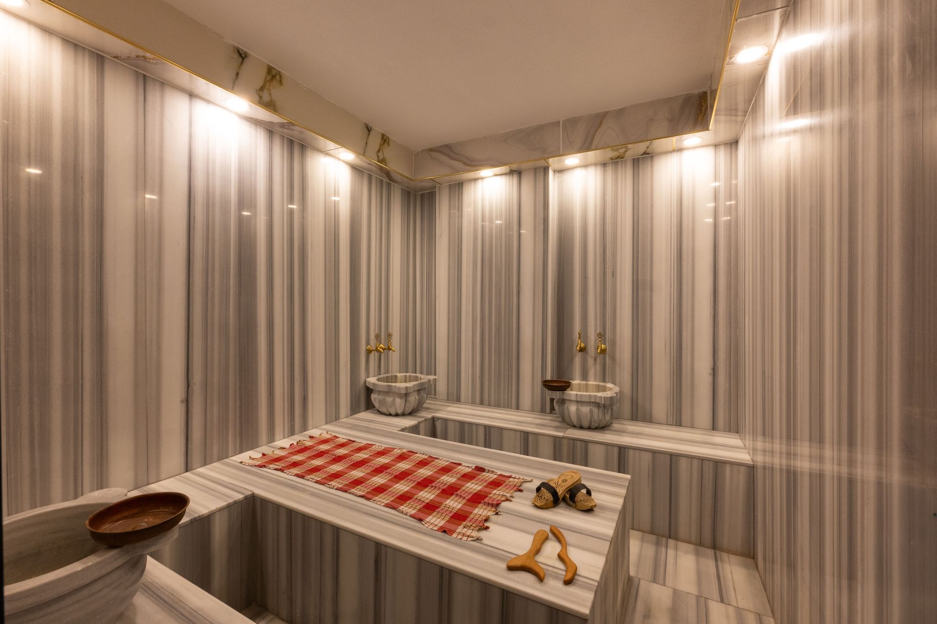 Mays Otel | Marble Turkish bath with two sinks, a red and white towel, and wooden sandals.