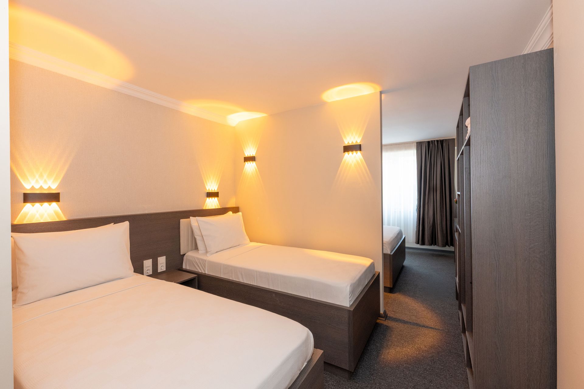 Mays Otel | Family Room | Twin beds in a neutral-toned hotel room, with wall sconce lighting.