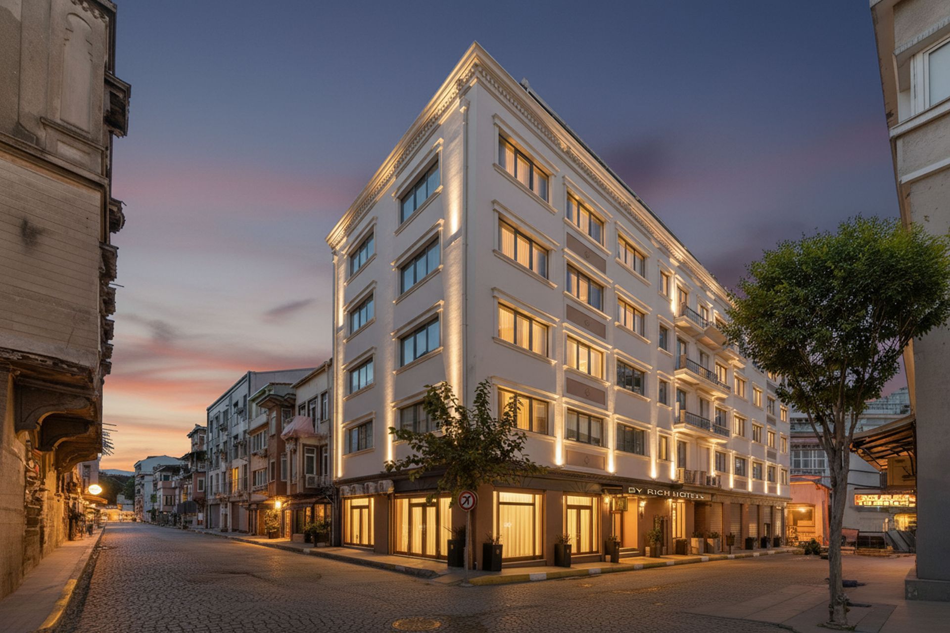 Mays Otel | Hotel building on a cobblestone street at dusk, lit with warm light.