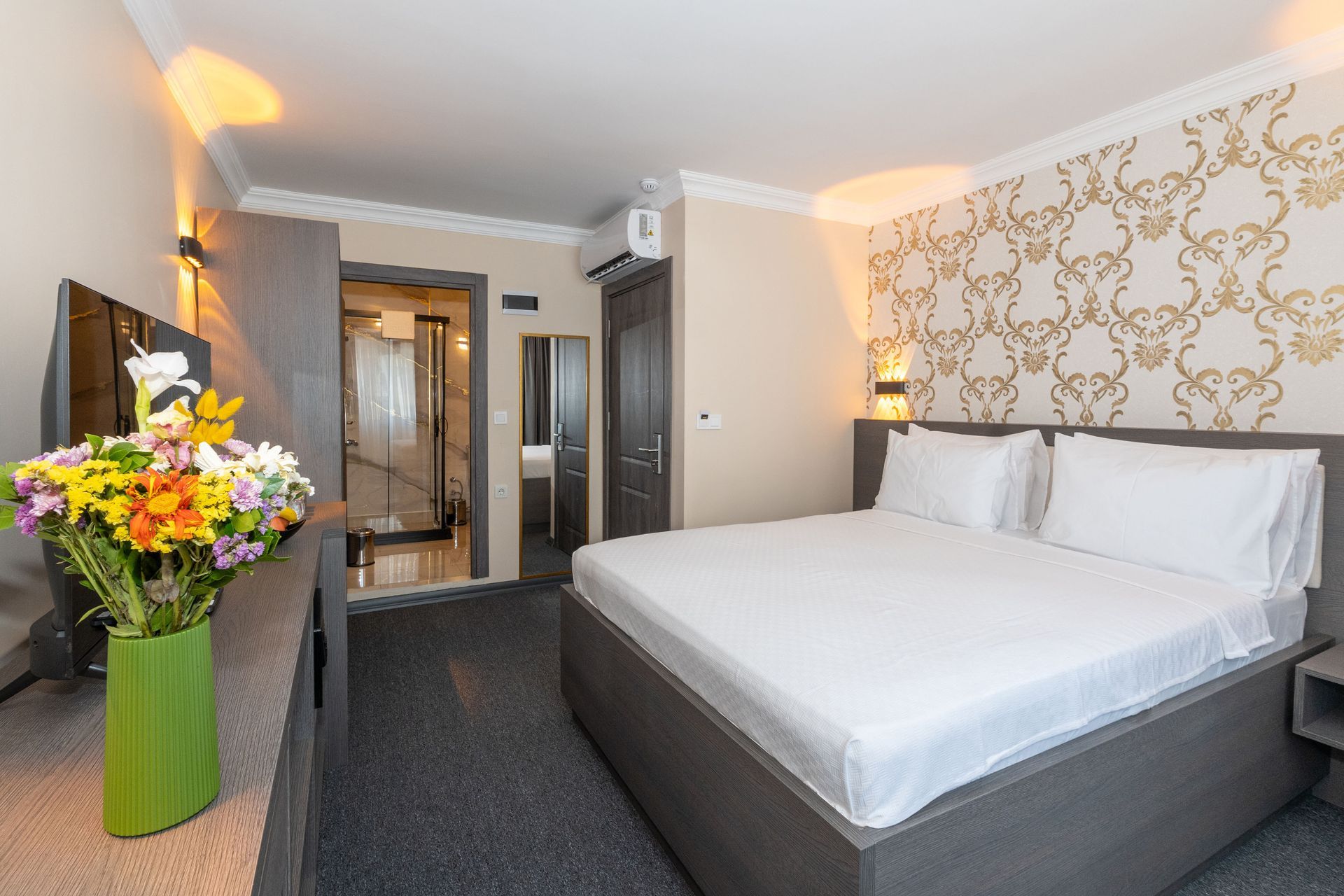 Mays Otel | Double Room | Hotel room with a bed, TV, flower bouquet, and patterned wallpaper.