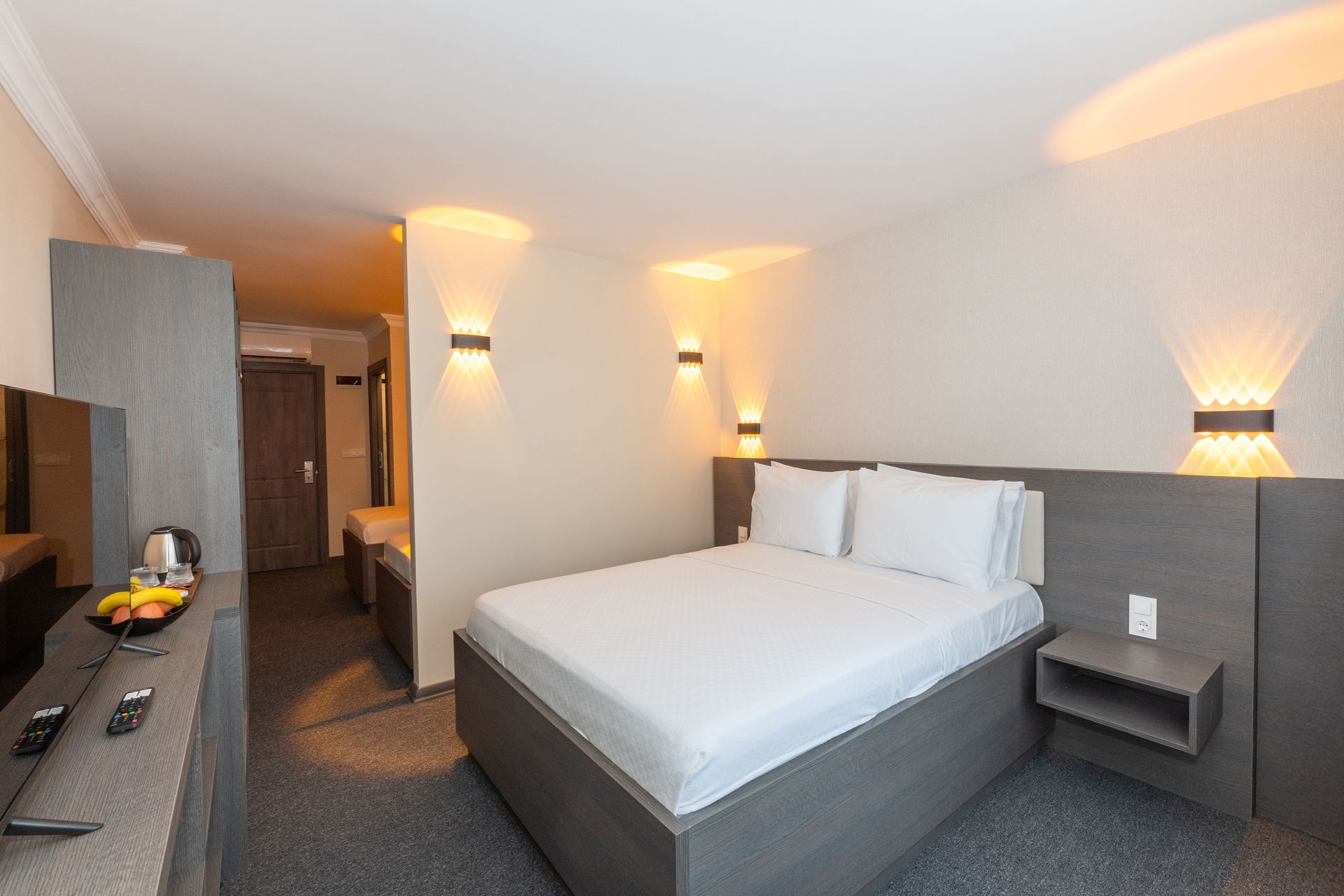 Mays Otel | Hotel bedroom with a bed, TV, and wardrobe, neutral colors, and decorative wall lights.