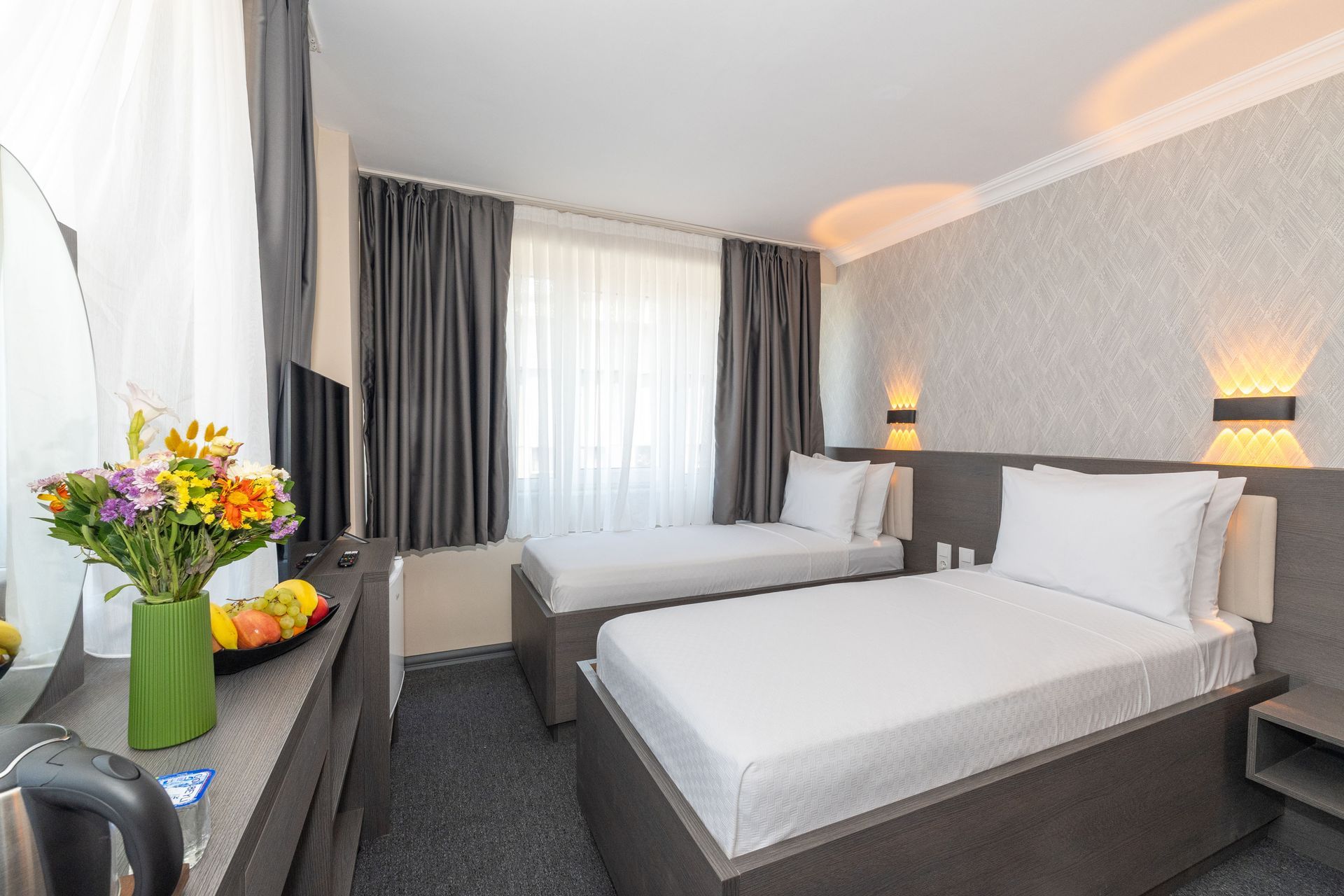 Mays Otel | Hotel room with two twin beds, gray curtains, and a vase of flowers.