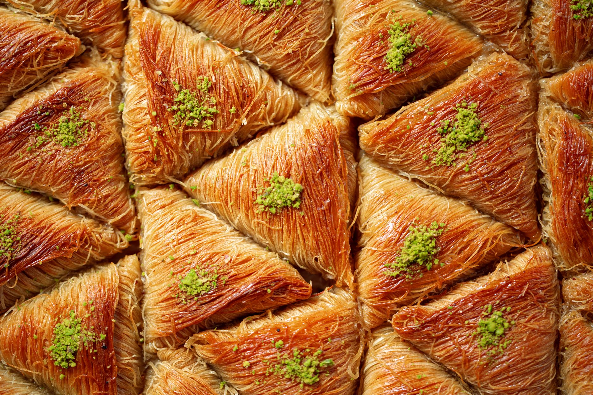 Mays Otel | Turkish Baklava | A triangular-shaped, golden brown dessert decorated with pistachios and grilled.