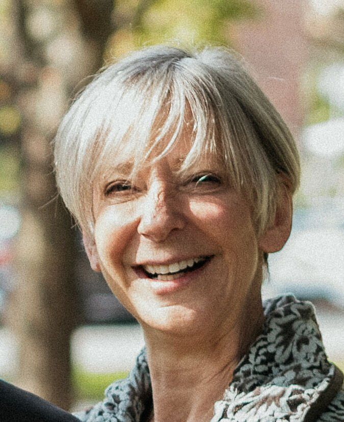 Smiling person with short silver hair outdoors, wearing a patterned scarf.