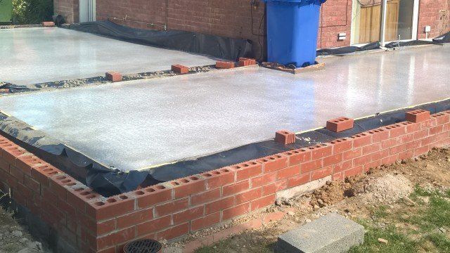 Brick foundation under construction with a concrete slab and a blue bin nearby