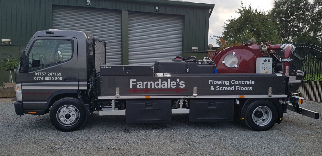 Gray utility truck with farmdale's logo, parked beside a building and a red water tank.