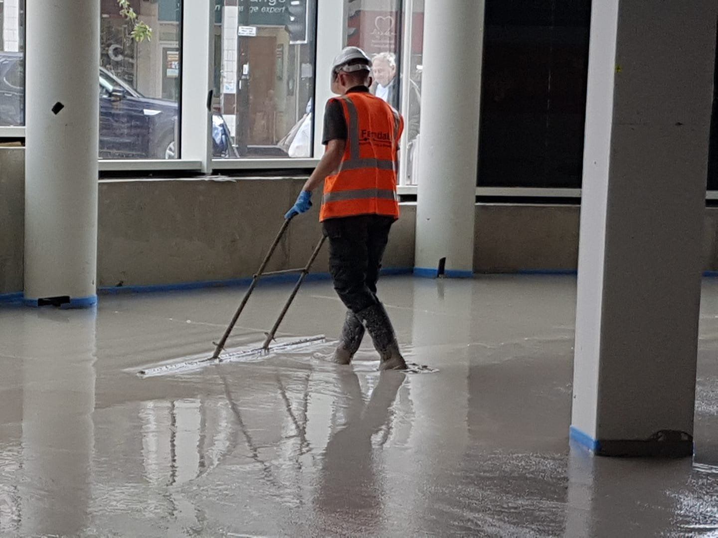 Person in an orange safety vest mopping a wet floor in a building lobby.