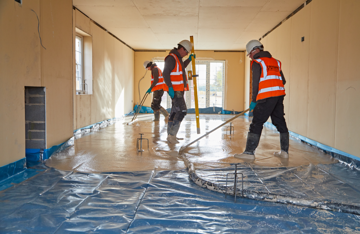 Workers in orange vests painting a room floor covered with blue protective sheeting.