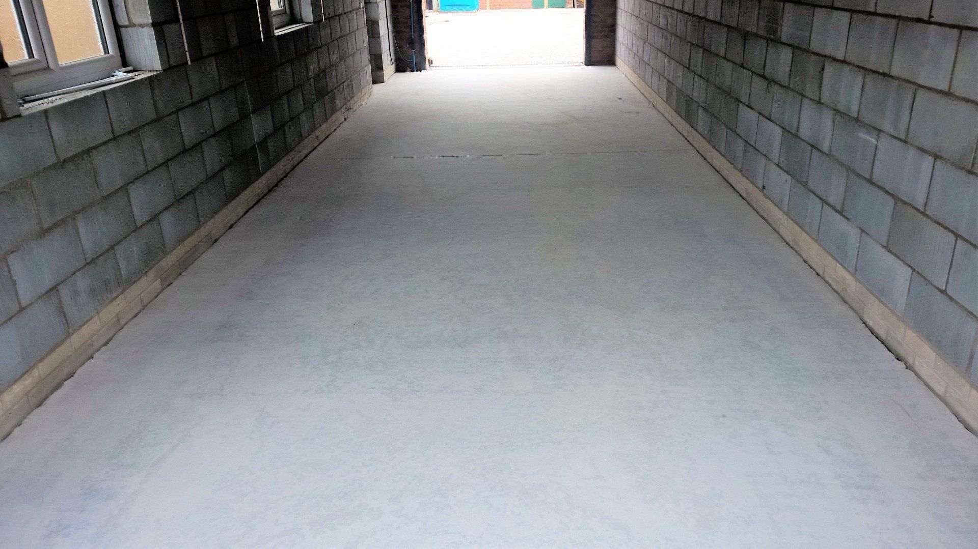 Empty concrete corridor with brick walls and bright light at the far end