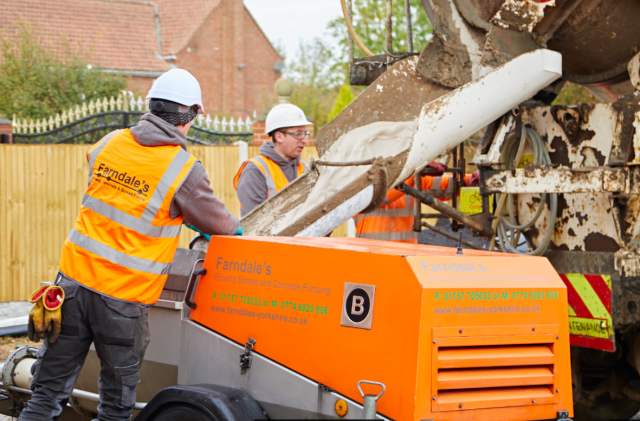 Construction workers operating an orange concrete mixer at a demolition site