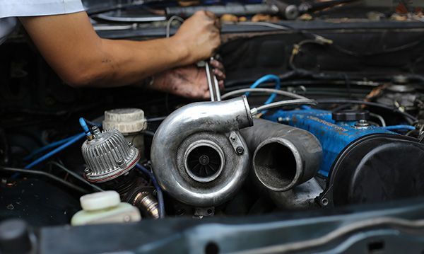 Person working on a car engine with a turbocharger installed. Hands use a wrench. | Auto Clinic Care