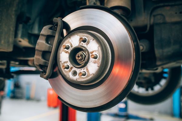 Car brake disc assembly, viewed from below, showing the rotor, caliper, and suspension components. | Auto Clinic Care