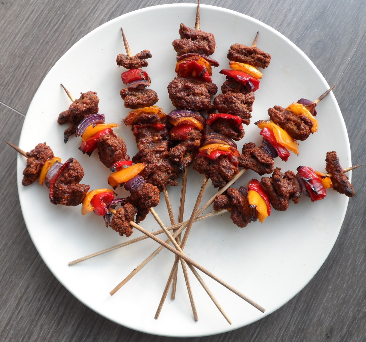 A bunch of skewers of meat and vegetables on a white plate.