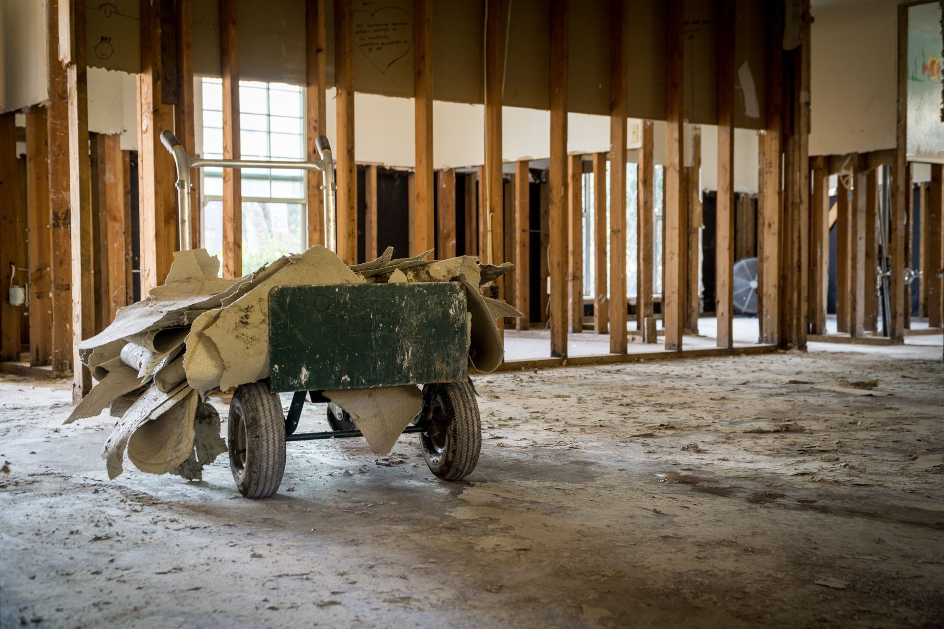 Hand truck loaded with debris inside a gutted building; wood framing visible.