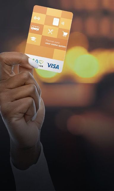 Mão segurando um cartão de crédito Visa dourado com ícones de aplicativos, contra um fundo quente desfocado.