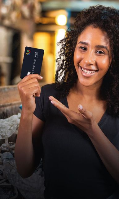 Mulher sorridente segurando um smartphone e apontando para ele em um ambiente interno com iluminação aconchegante.