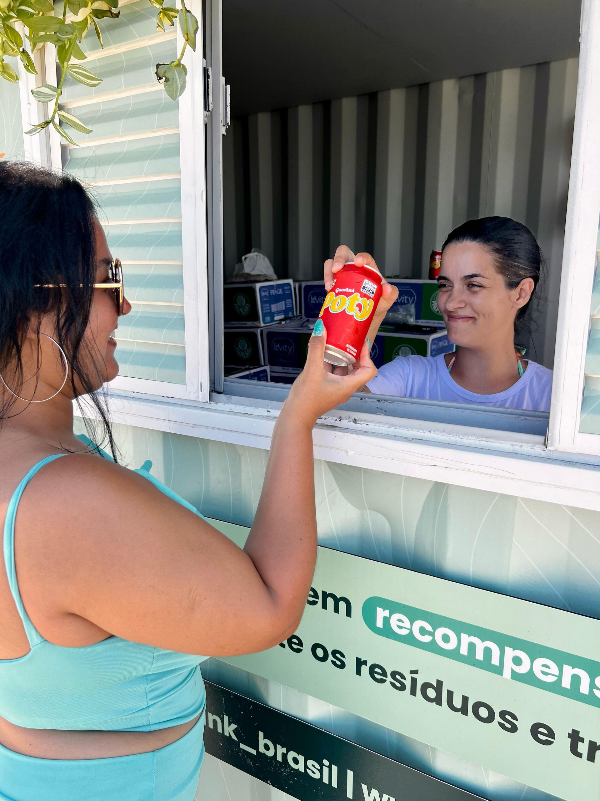 Uma pessoa entrega um copo vermelho de lanche a uma mulher em uma janela de atendimento.