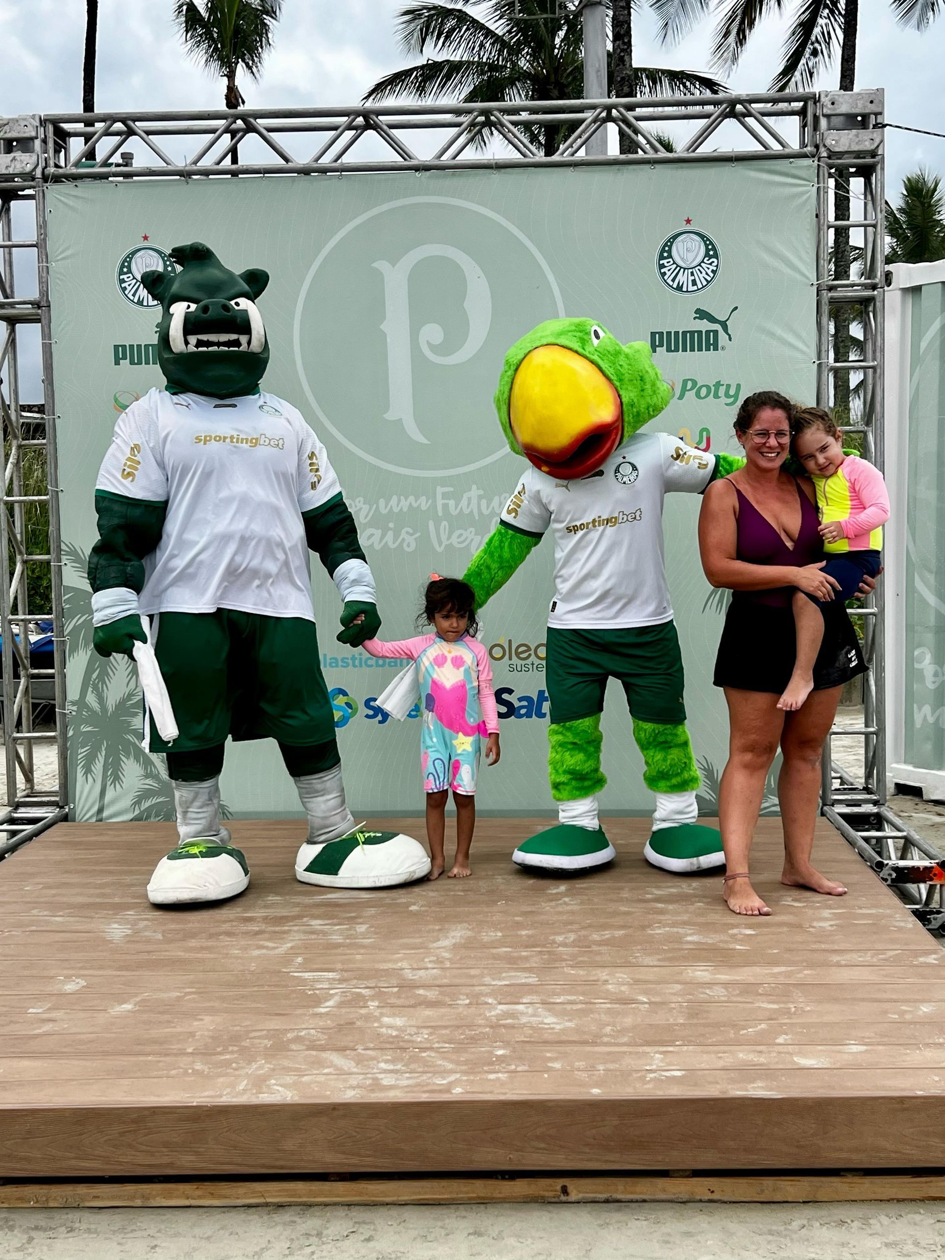 Personagens mascotes posando com uma criança e um adulto em um palco ao ar livre em um evento da PUMA.