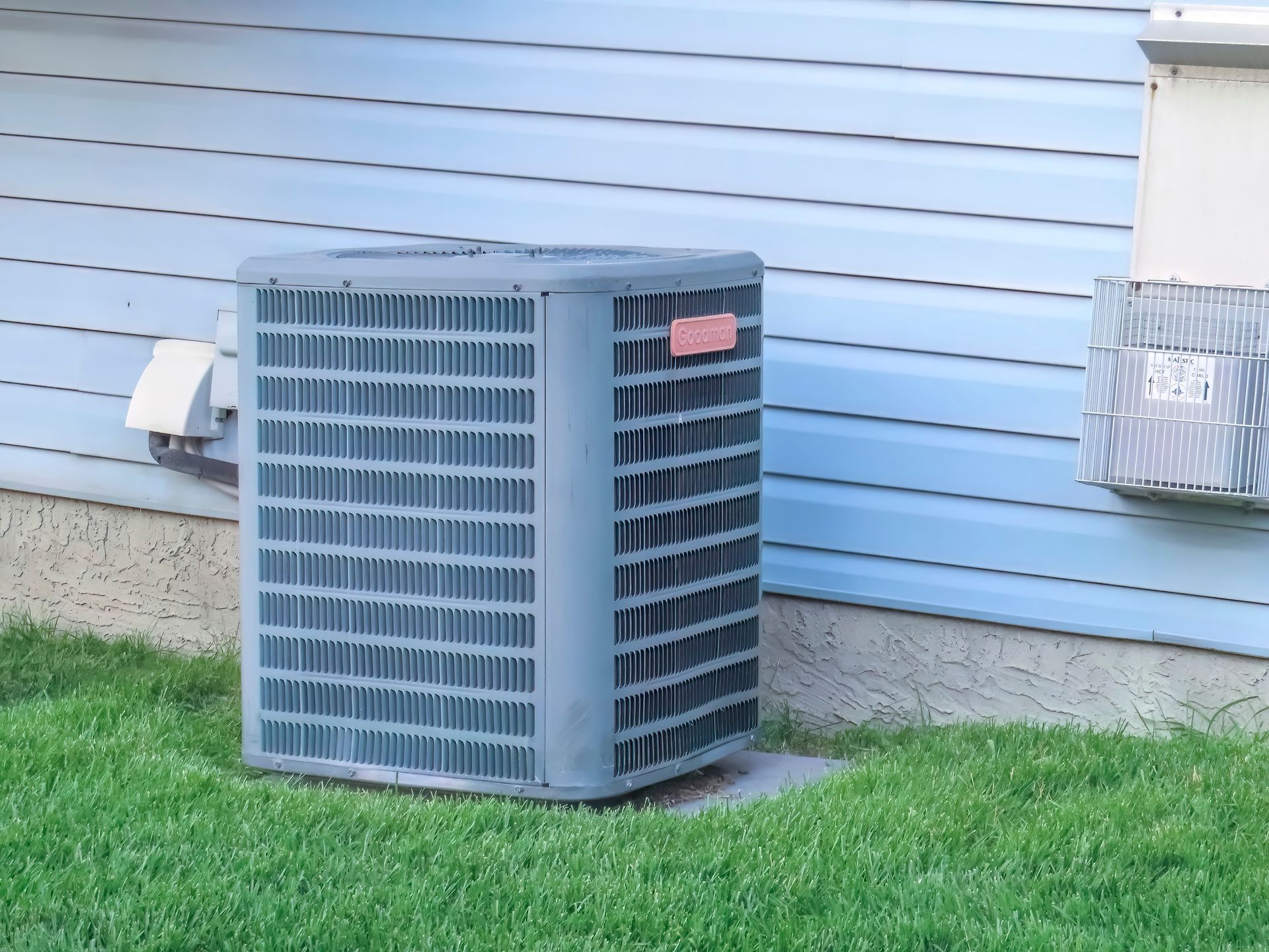 Outdoor air conditioner unit beside a house with blue siding and green lawn