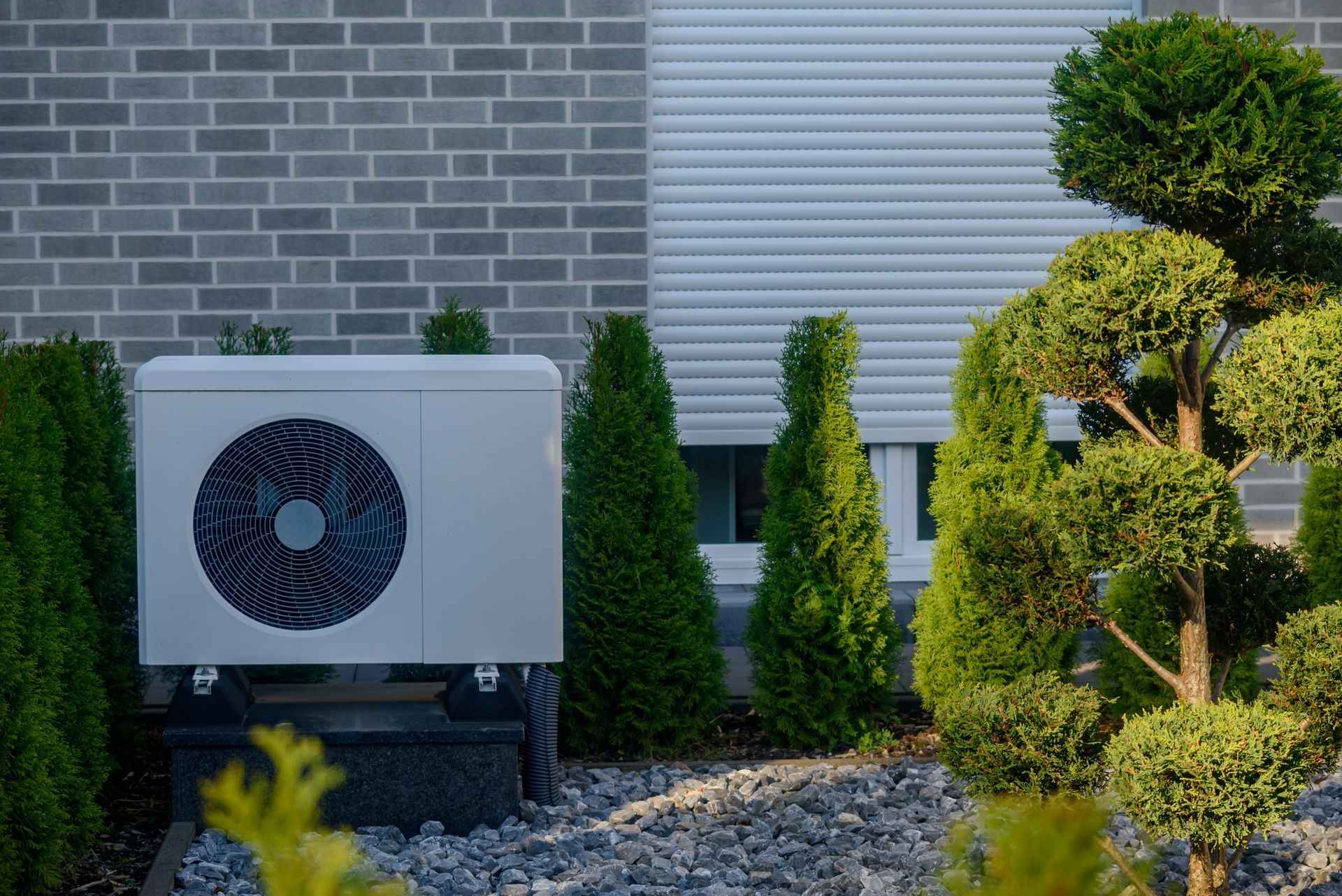 Outdoor air conditioning unit beside brick wall and shrubs in a landscaped yard